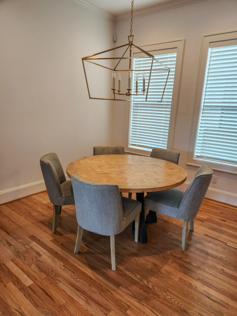 Modern dining area featuring a round wooden table surrounded by four upholstered chairs, with large windows and a stylish